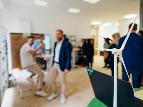 Menschen unterhalten sich im Hintergrund. Im Vordergrund steht das Modell eines Windrades.