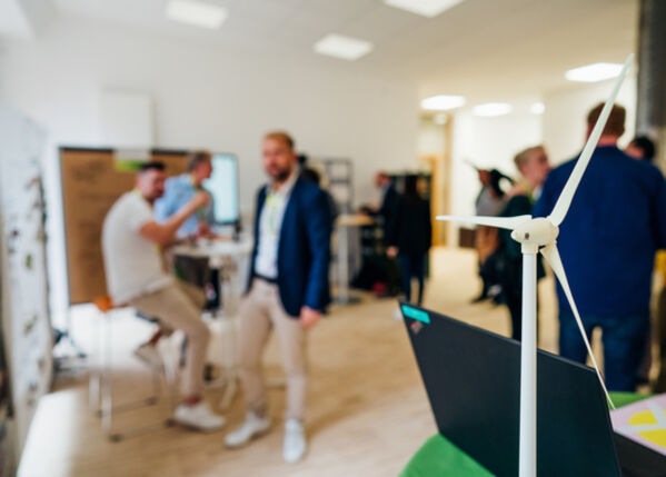 Menschen unterhalten sich im Hintergrund. Im Vordergrund steht das Modell eines Windrades.