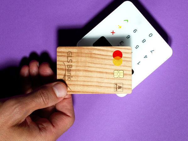 Das Bild zeigt die GLS Holzbankkarte auf ein Kartenlesegerät gehalten wird.